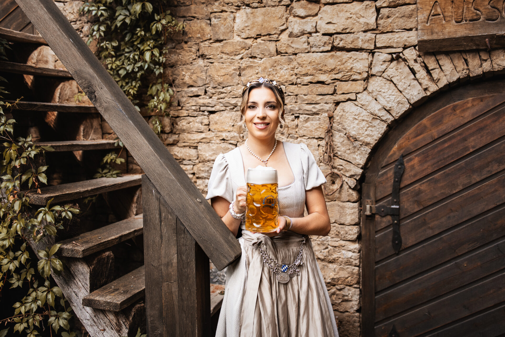 Junge, schöne Frau im Dirndl mit Krone und einem frisch eingeschenkten Maß Bier. Auf dem Maßkrug ist das Logo Bayerisches Bier zu erkennen. Sie lächelt in die Kamera.